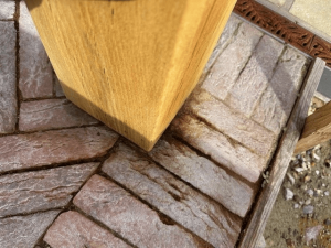 Oak post standing on paving with brown tannin stains around its base.