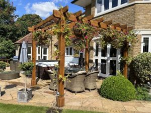 An oak pergola with tenoned lattice panels supporting blooming climbing roses.