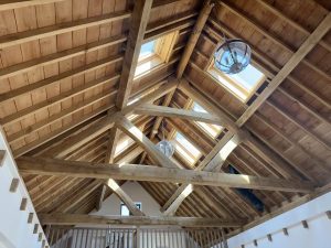 Interior view of a barn with a green oak queen post truss, highlighting the expansive space created by the timber frame design